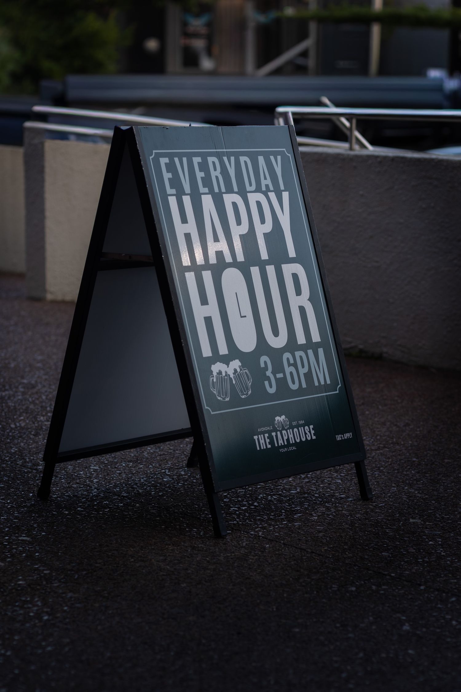 A-frame sidewalk sign displaying happy hour times outside a bar.