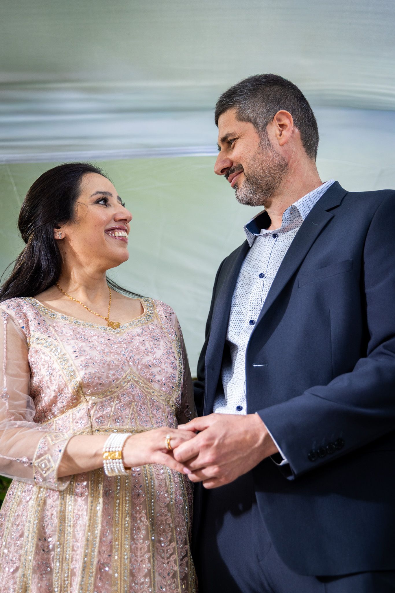 Couple in formal attire holding hands and smiling at each other during a wedding ceremony.