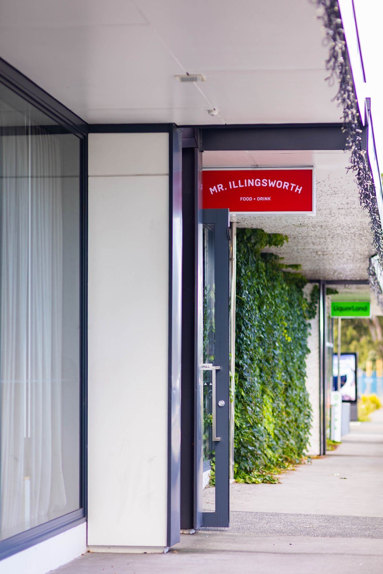 Modern office hallway with white walls, glass panels, and vertical green plant installations along the corridor.