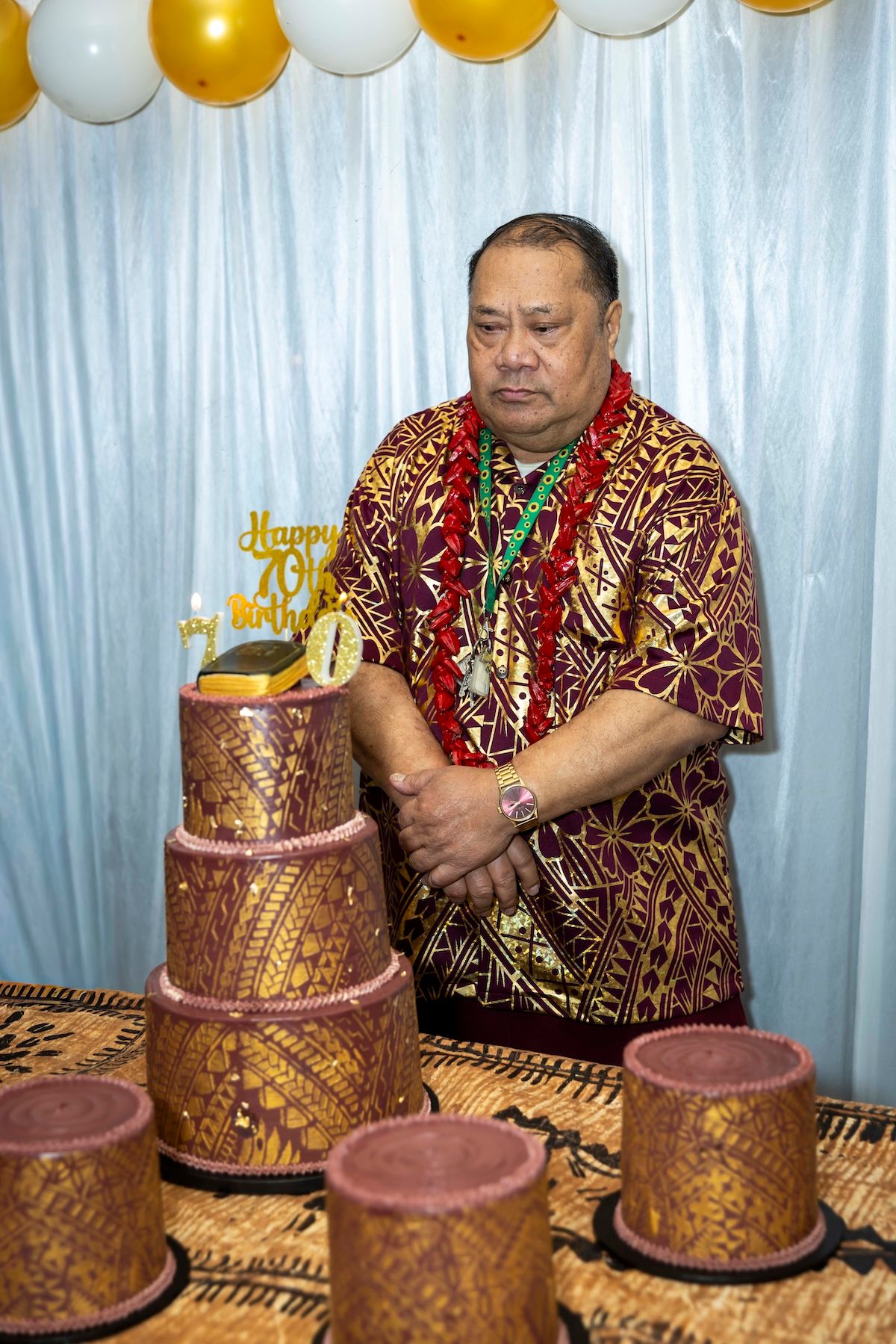 Elegant gold and brown tiered celebration cakes with intricate designs displayed at a party with gold and white balloons.