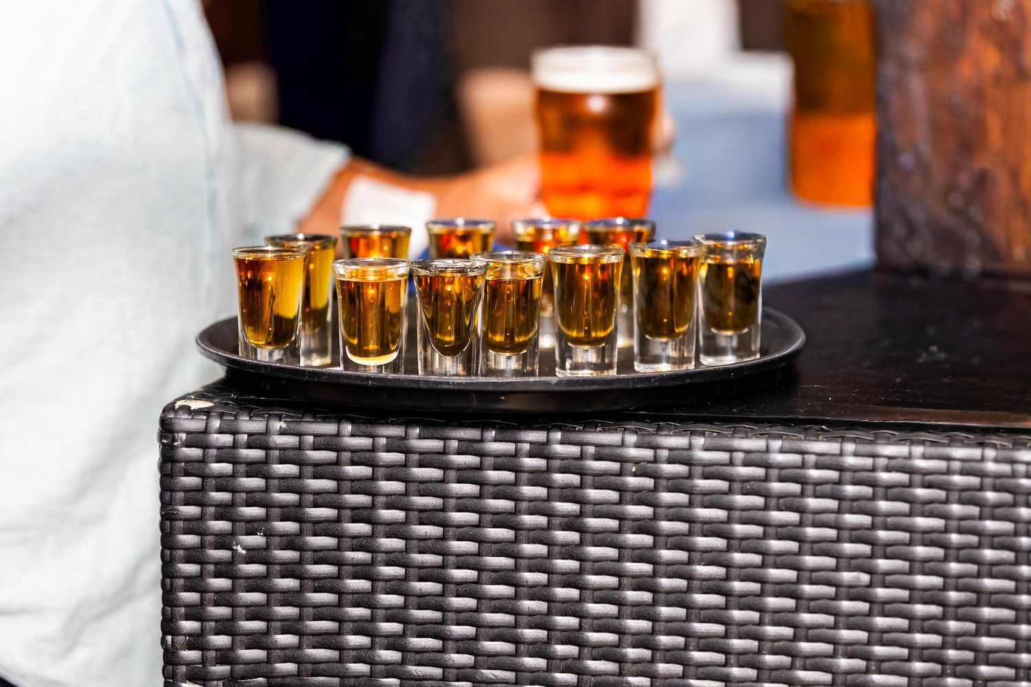 A tray of golden whiskey shot glasses arranged on a wicker table at a bar event.