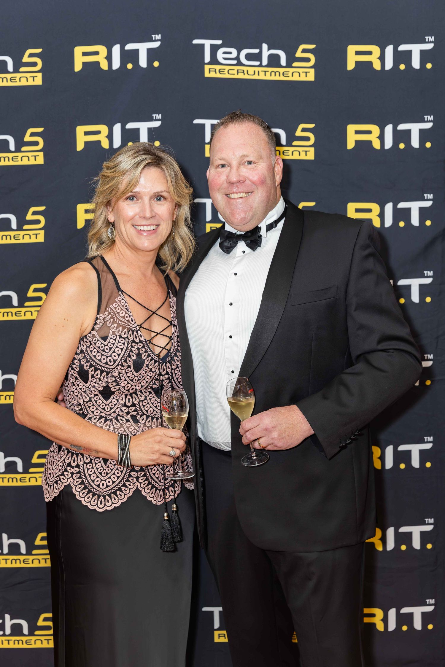 A couple in formal attire holding champagne glasses at a Tech 5 Recruitment and R.I.T. corporate event.
