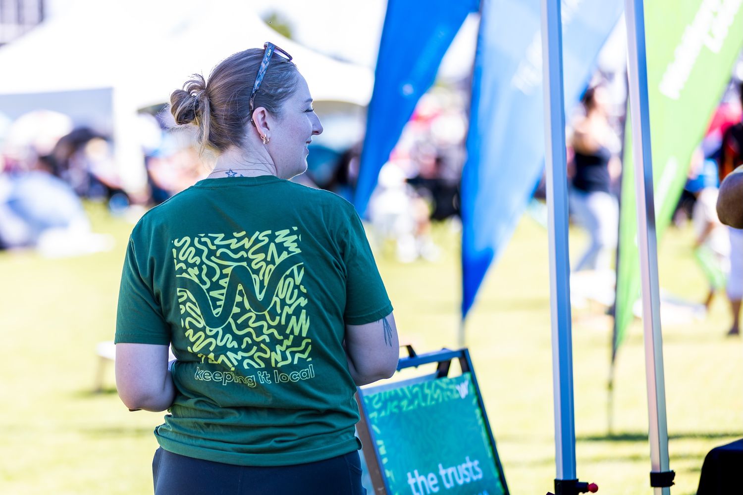 Volunteers in green t-shirts managing a booth at a sunny outdoor festival.