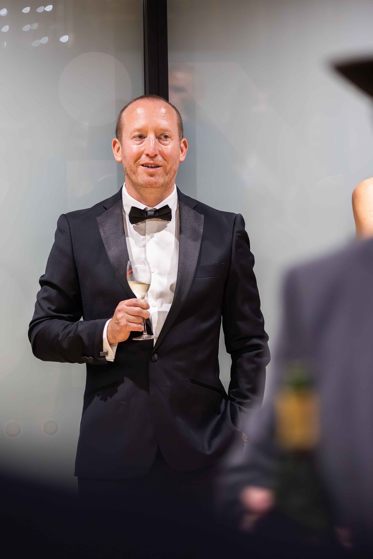 Elegant man in black tuxedo with bow tie holding champagne glass at formal event.