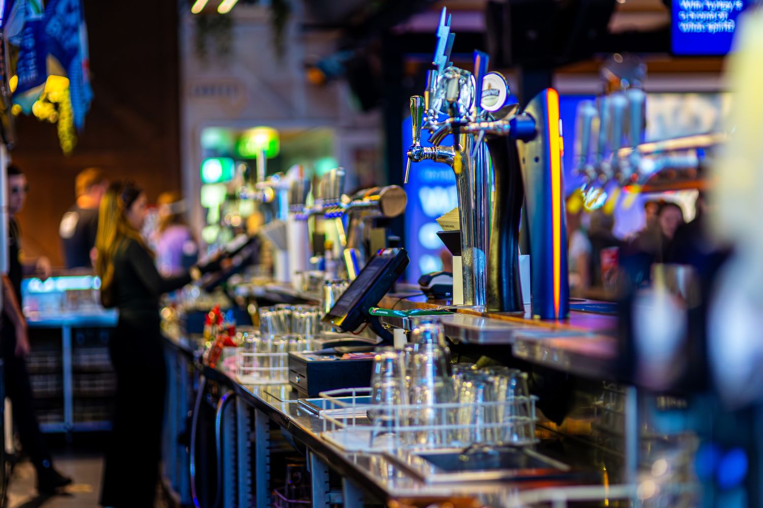 Illuminated bar counter with glowing blue lights and glass bottles on display in a dimly lit nightclub atmosphere.