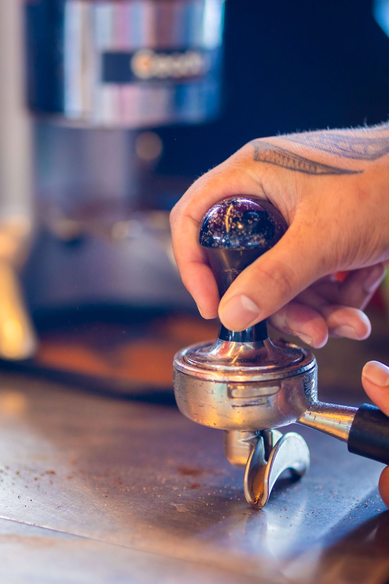 Close-up shot of hands using a coffee tamper to compress espresso grounds in a metal portafilter.