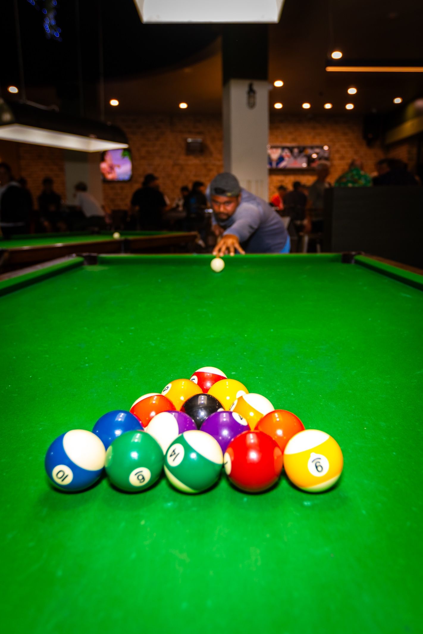 Colorful billiard balls arranged in a line on a green felt pool table with warm ambient lighting in the background.