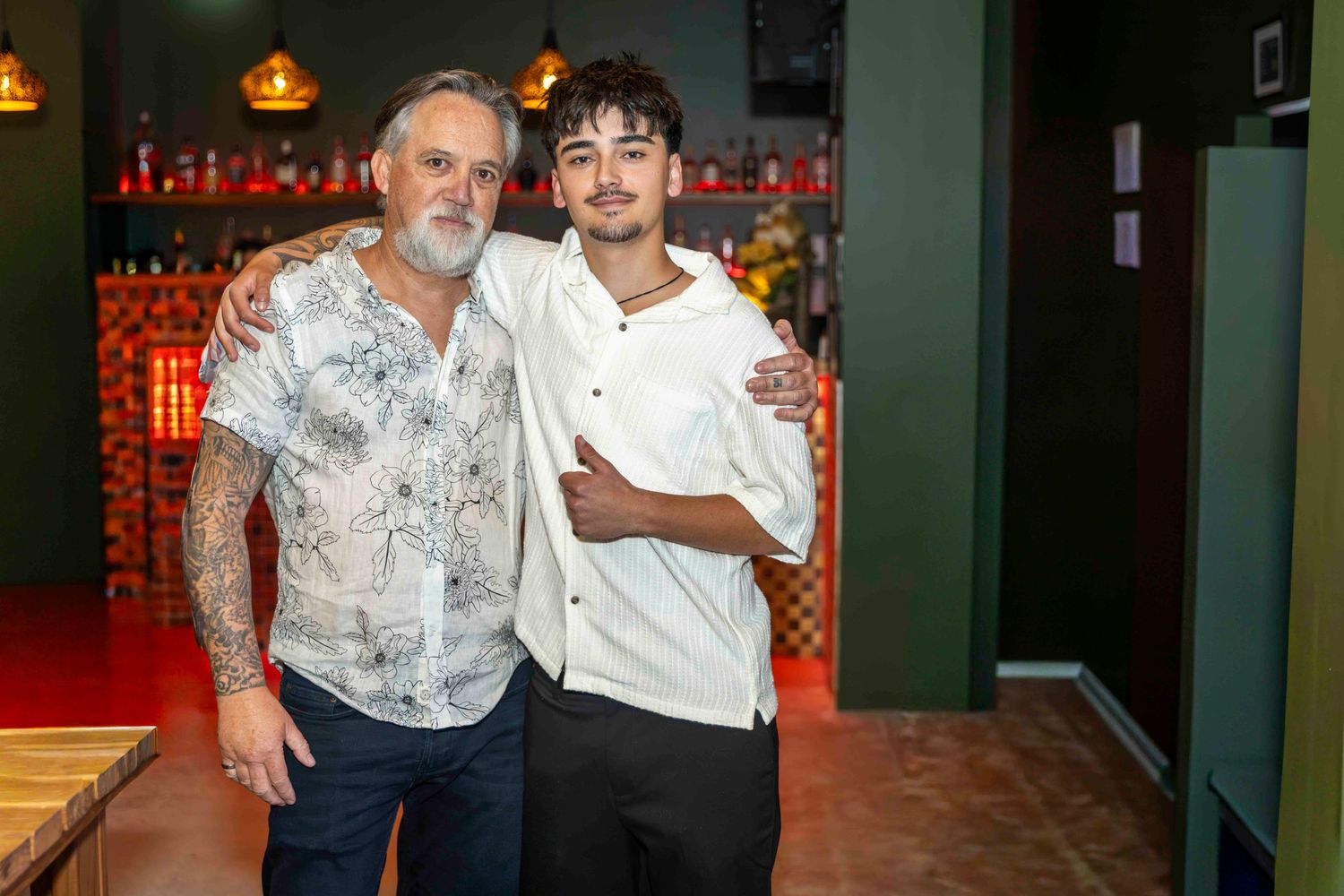 Two men smiling and posing together inside a modern restaurant with green walls and warm lighting.