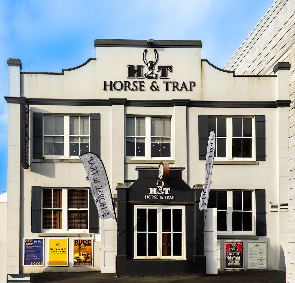 Exterior of Horse & Trap pub with white facade, black trim, banner flags, and classic signage on a bright day.
