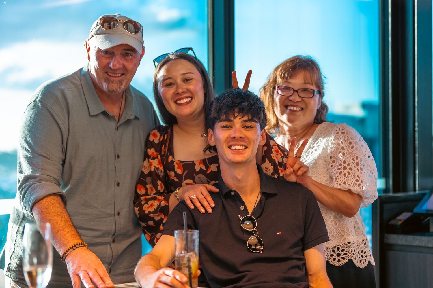 Four people smiling and posing together at a restaurant with scenic views, enjoying drinks and celebrating a special occasion.
