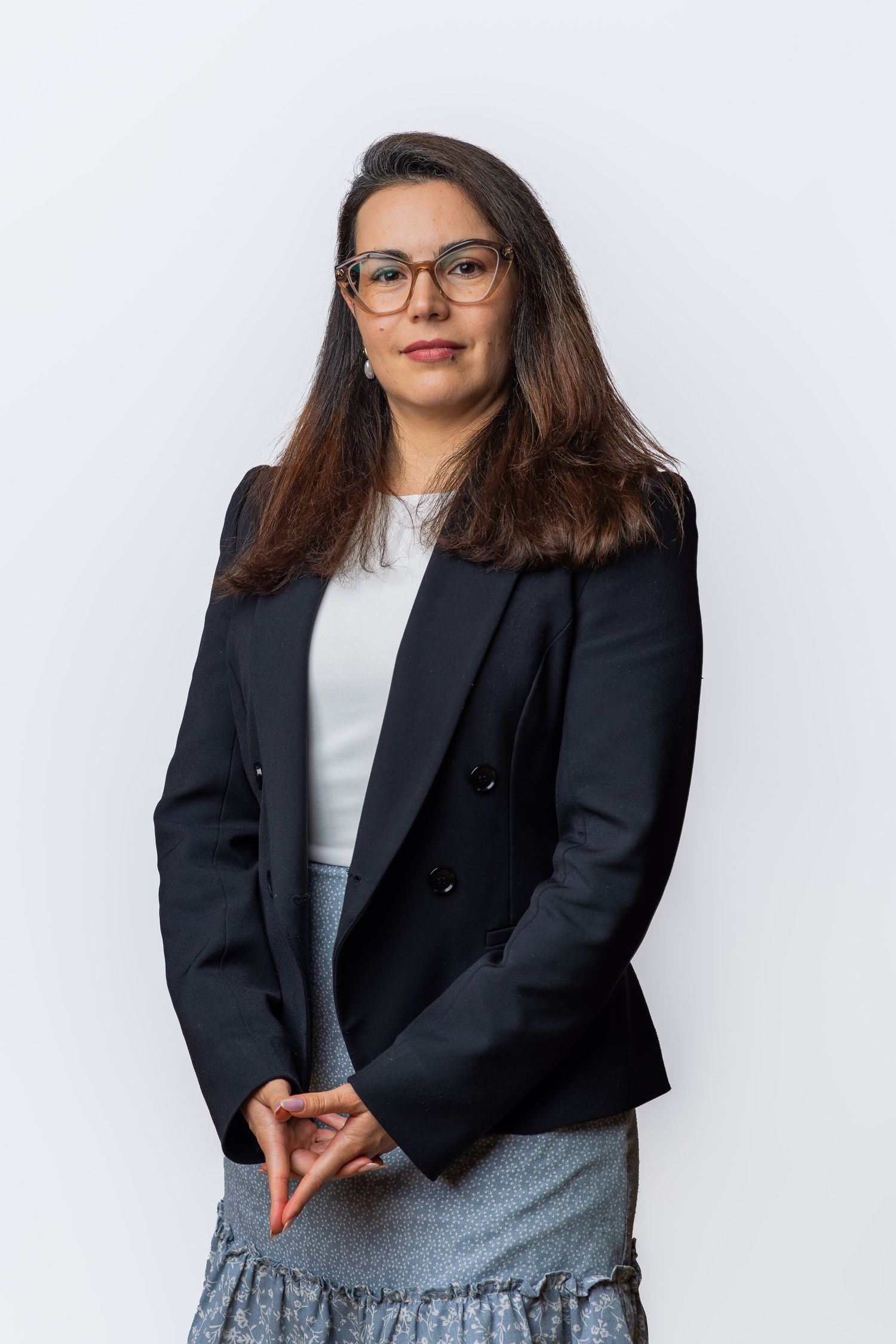 Professional woman in black blazer and glasses posing against white background for business portrait.