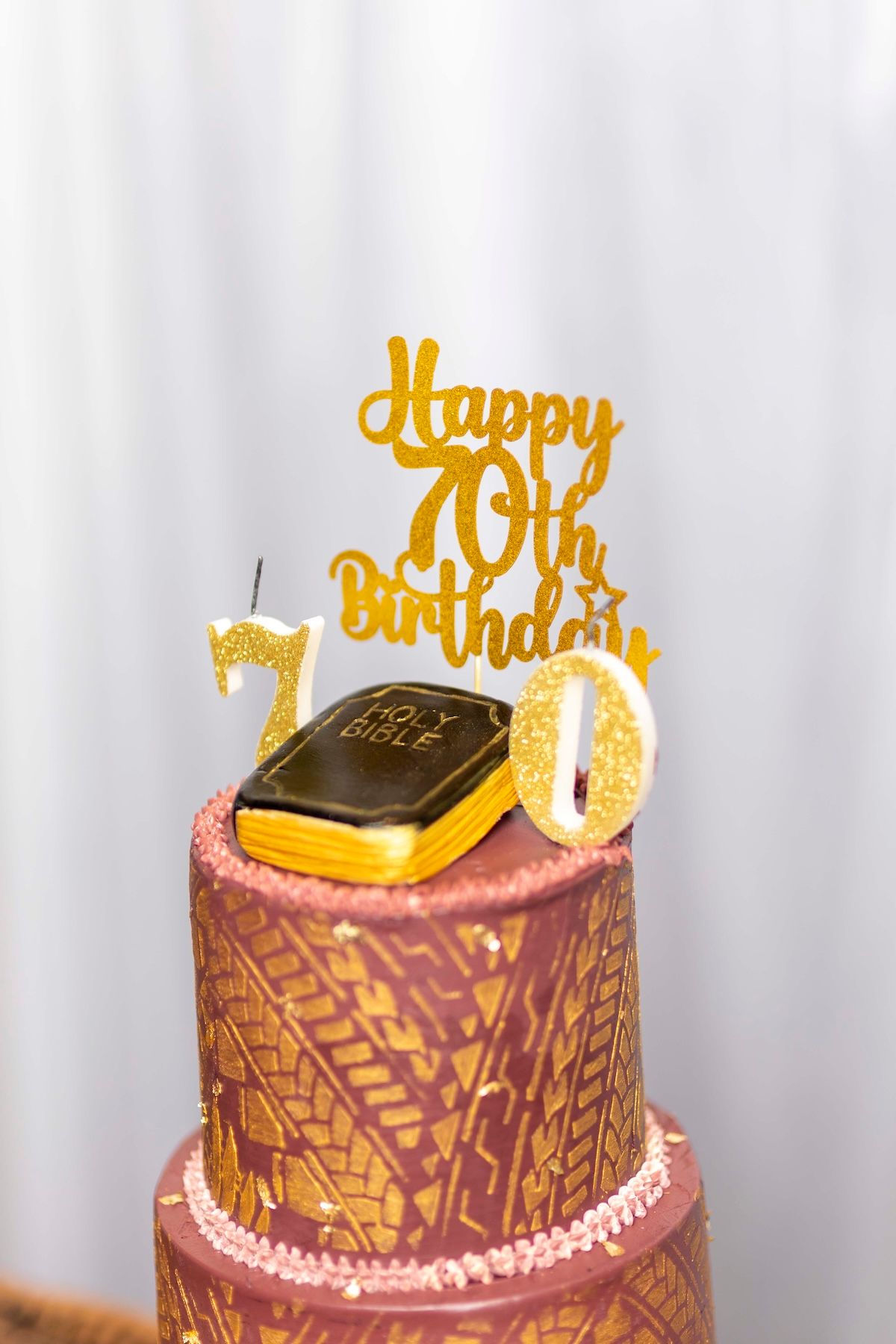 A two-tiered pink and brown birthday cake decorated with gold accents and a 'Happy Birthday' topper.