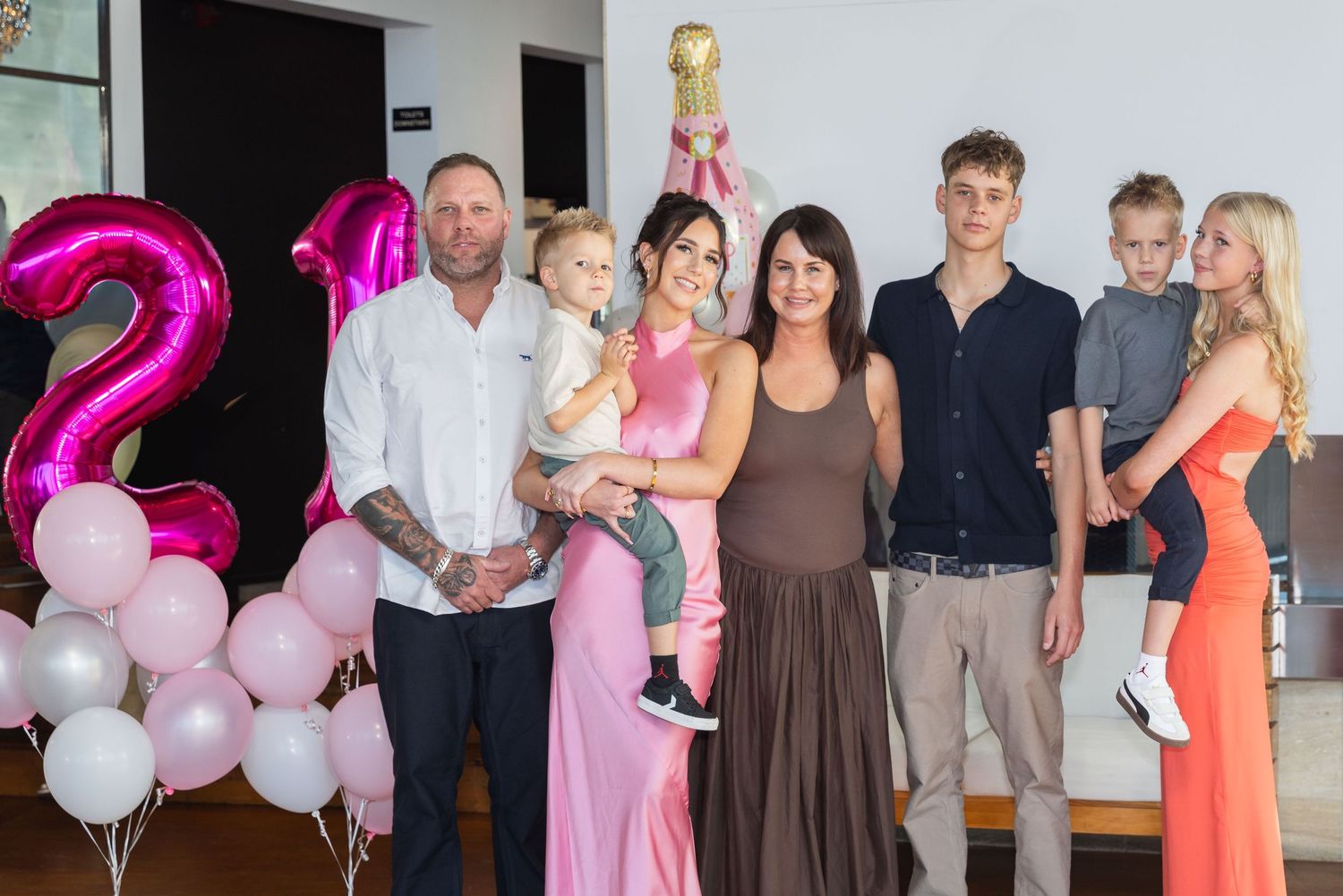 Family group photo at a birthday party with pink balloons and number 2 decoration, celebrating a child's second birthday.