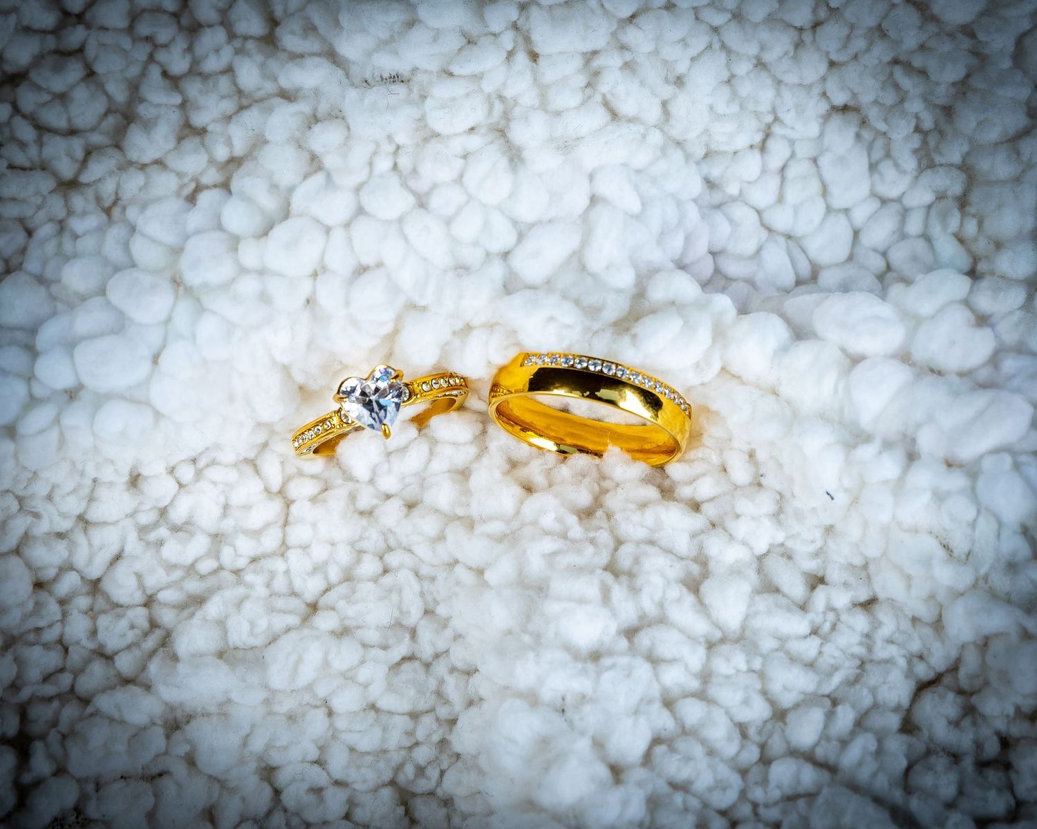 Two gold rings, one with a diamond solitaire, resting on a white textured surface.