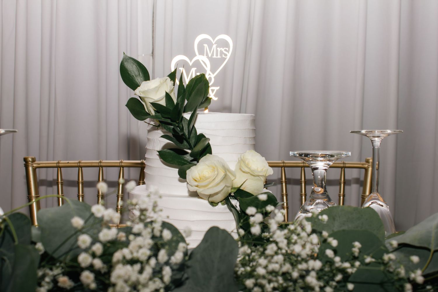 Elegant white wedding cake display with fresh roses and greenery against a light backdrop.