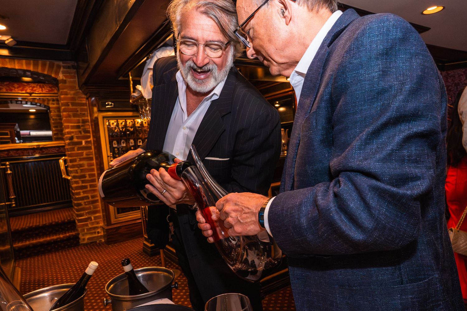 Two men examining a wine bottle at an upscale restaurant bar setting.
