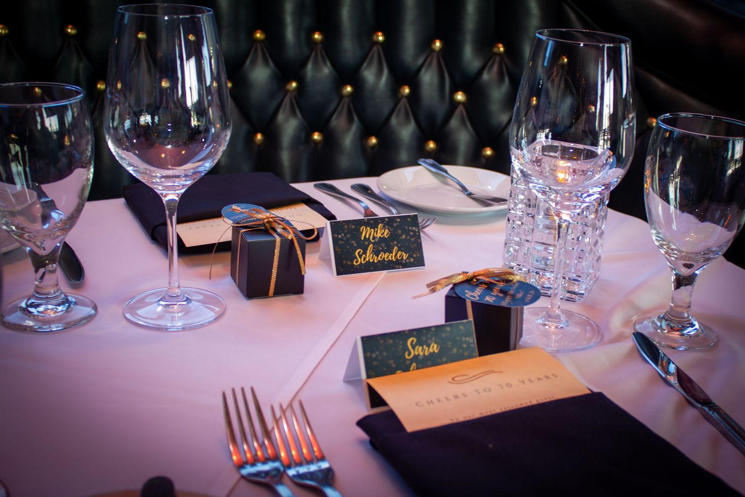 Elegant wedding reception table setting with place cards, black gift boxes, crystal glassware, and pink tablecloth.