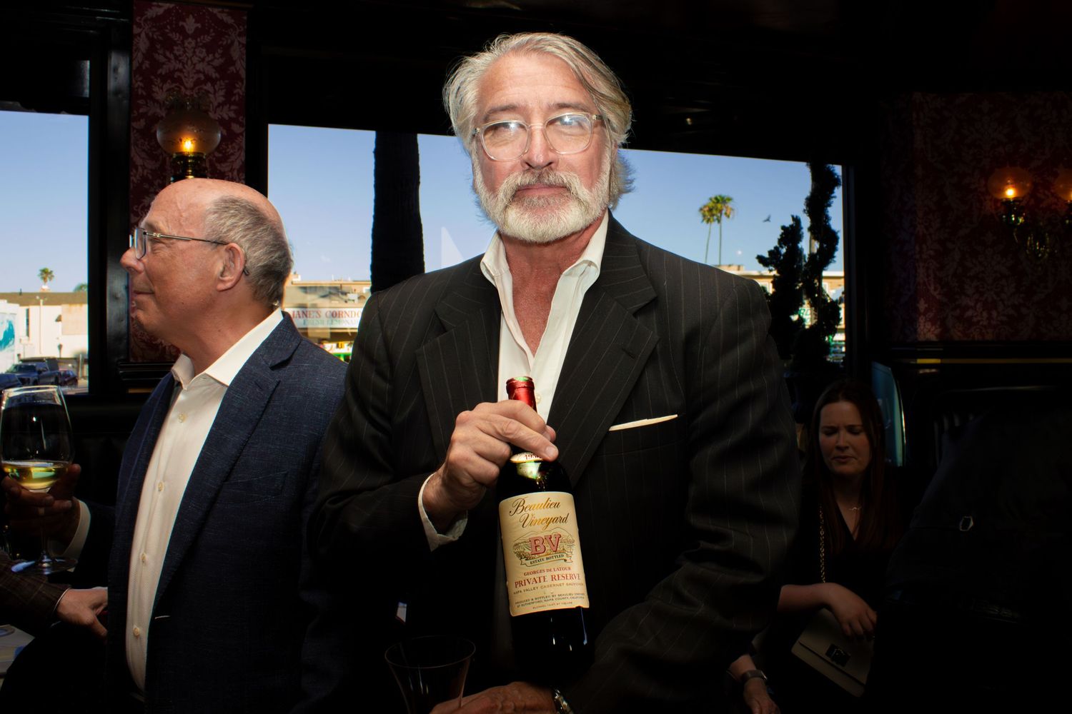 Man holding a wine bottle at an upscale restaurant event with harbor views in the background.