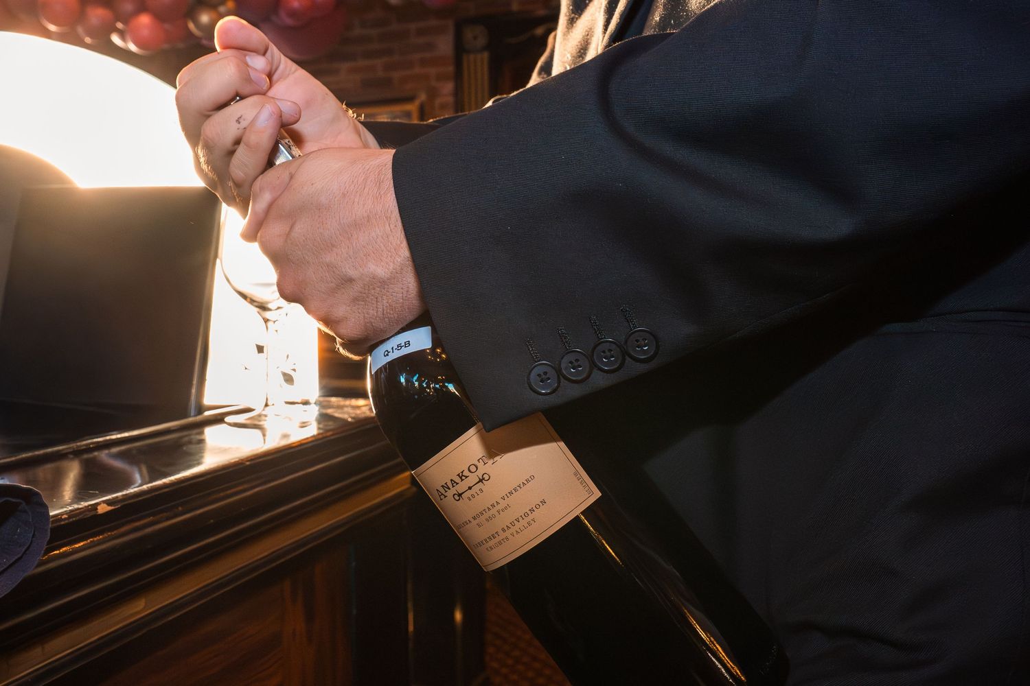A sommelier in a dark suit opens a wine bottle at an upscale restaurant bar with warm ambient lighting.