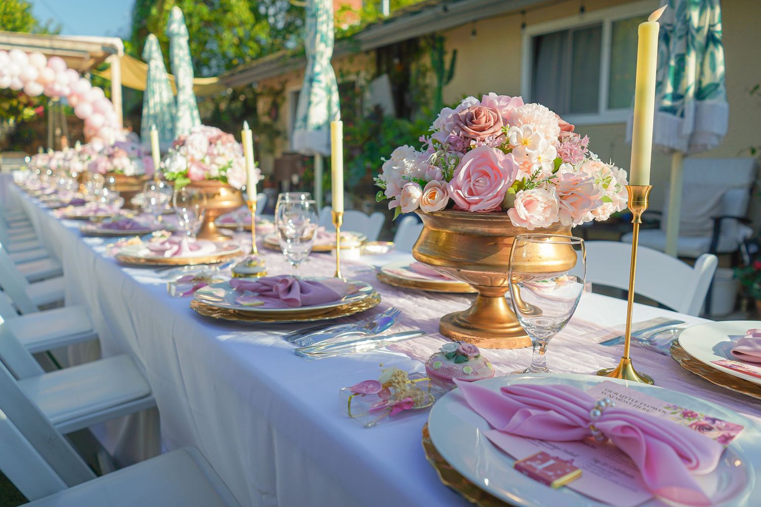 Elegant outdoor table settings with pink floral centerpieces and gold accents for a garden wedding.