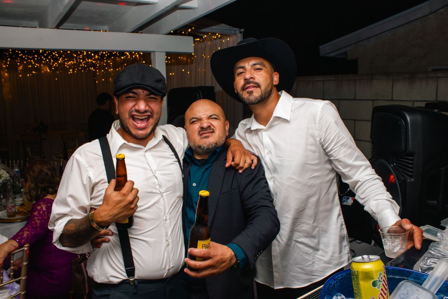 Wedding party members in formal attire celebrate with drinks and smiles at an indoor reception.