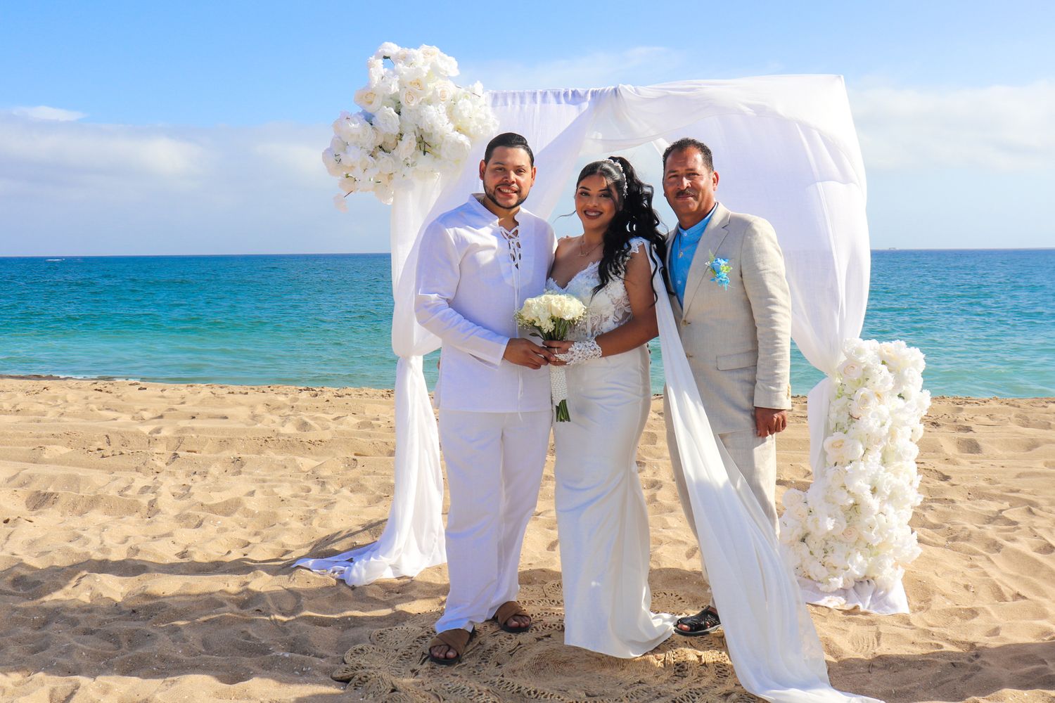 Romantic beach wedding scene with white floral arrangements and crystal blue waters.