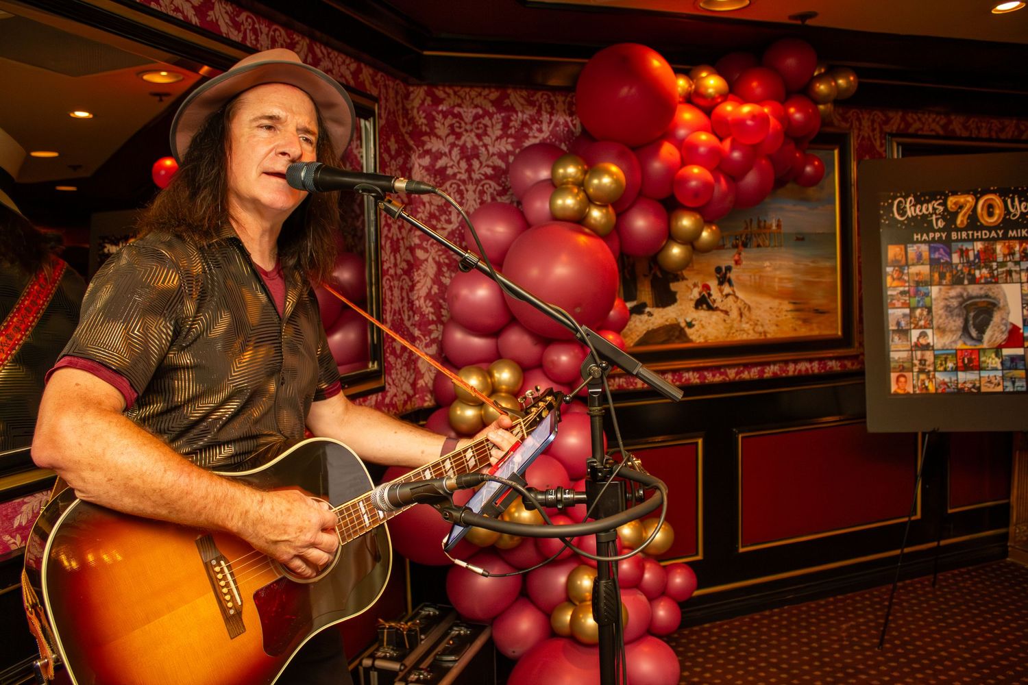 A guitarist performs in front of red and gold balloon decorations at a restaurant event.
