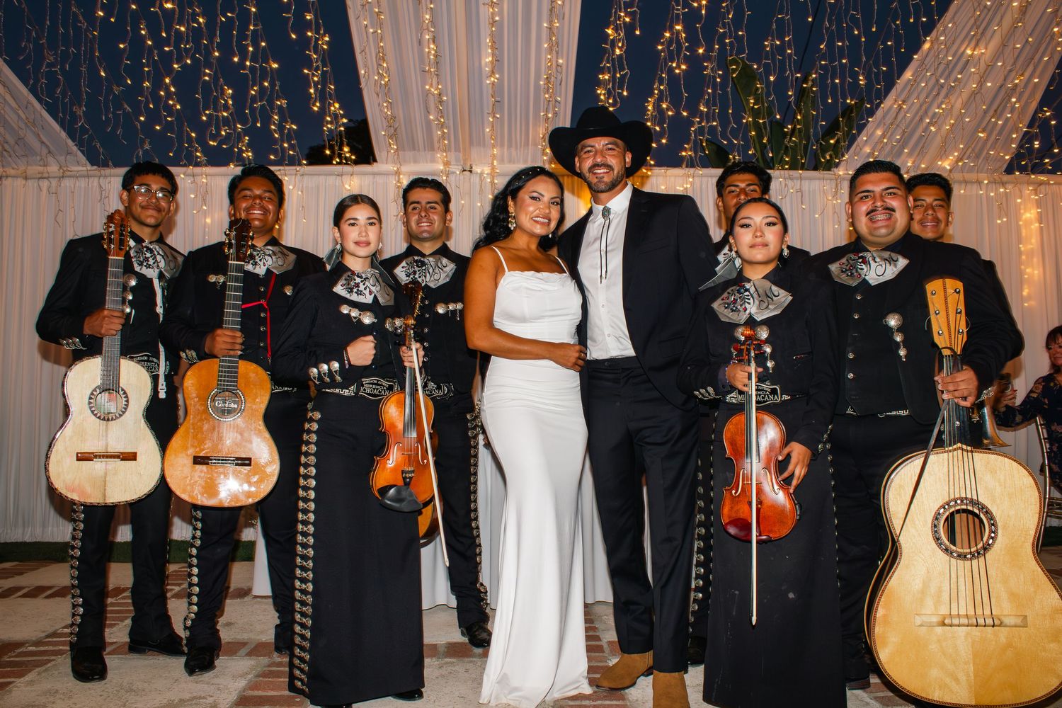 A mariachi band performing at a wedding celebration with guitars and traditional outfits.