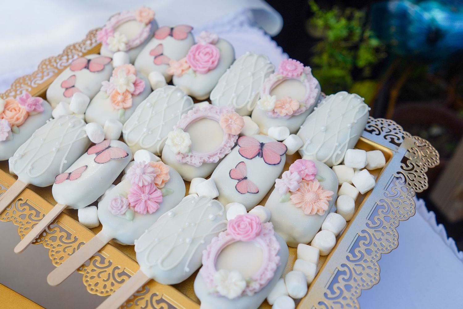 White chocolate covered cake pops decorated with pink flowers on gold lace stands.