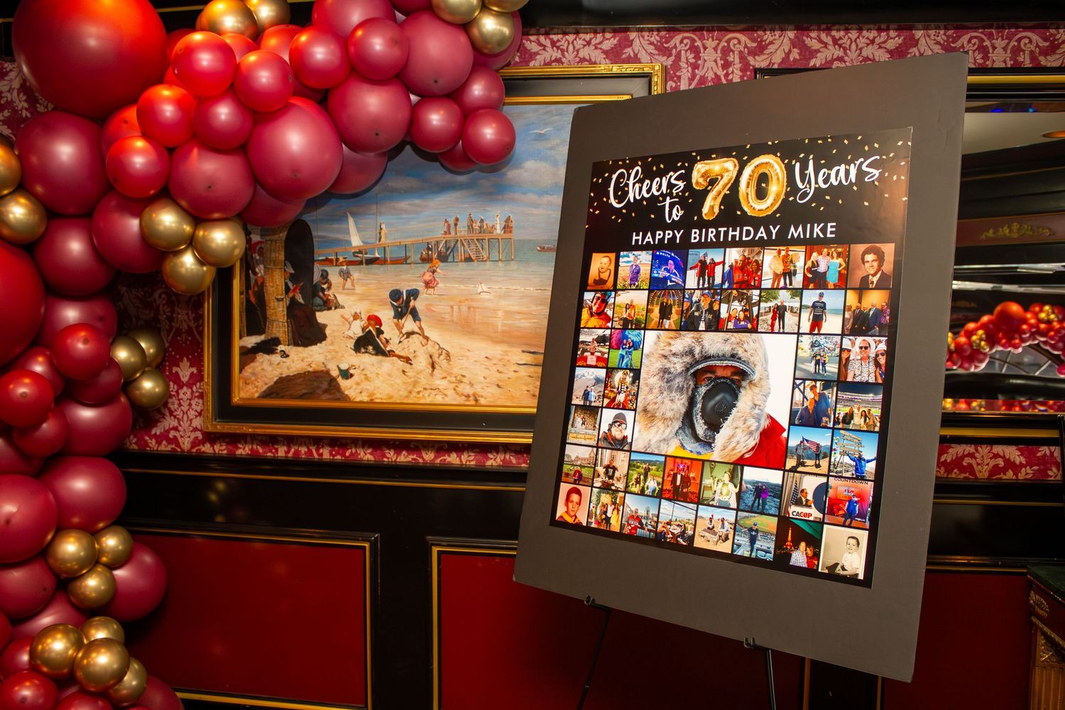 70th birthday party display with red and gold balloon arch and photo collage sign reading Cheers to 70 Years Happy Birthday Mike.