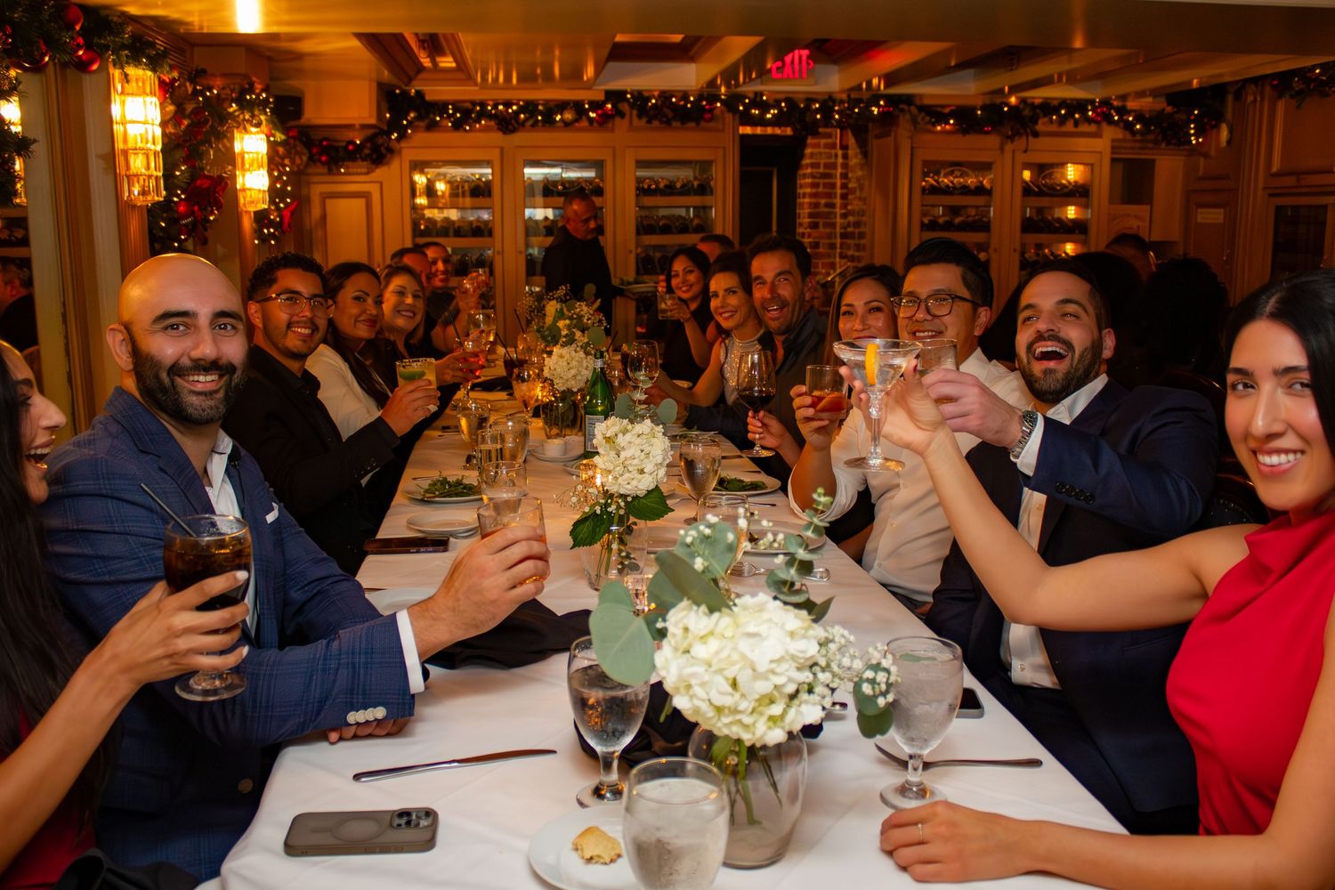 Wedding reception guests raise their glasses in a toast around an elegantly decorated dining table.