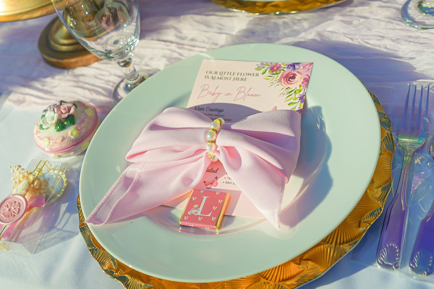 Elegant place setting with mint green plate and pink bow on gold charger.