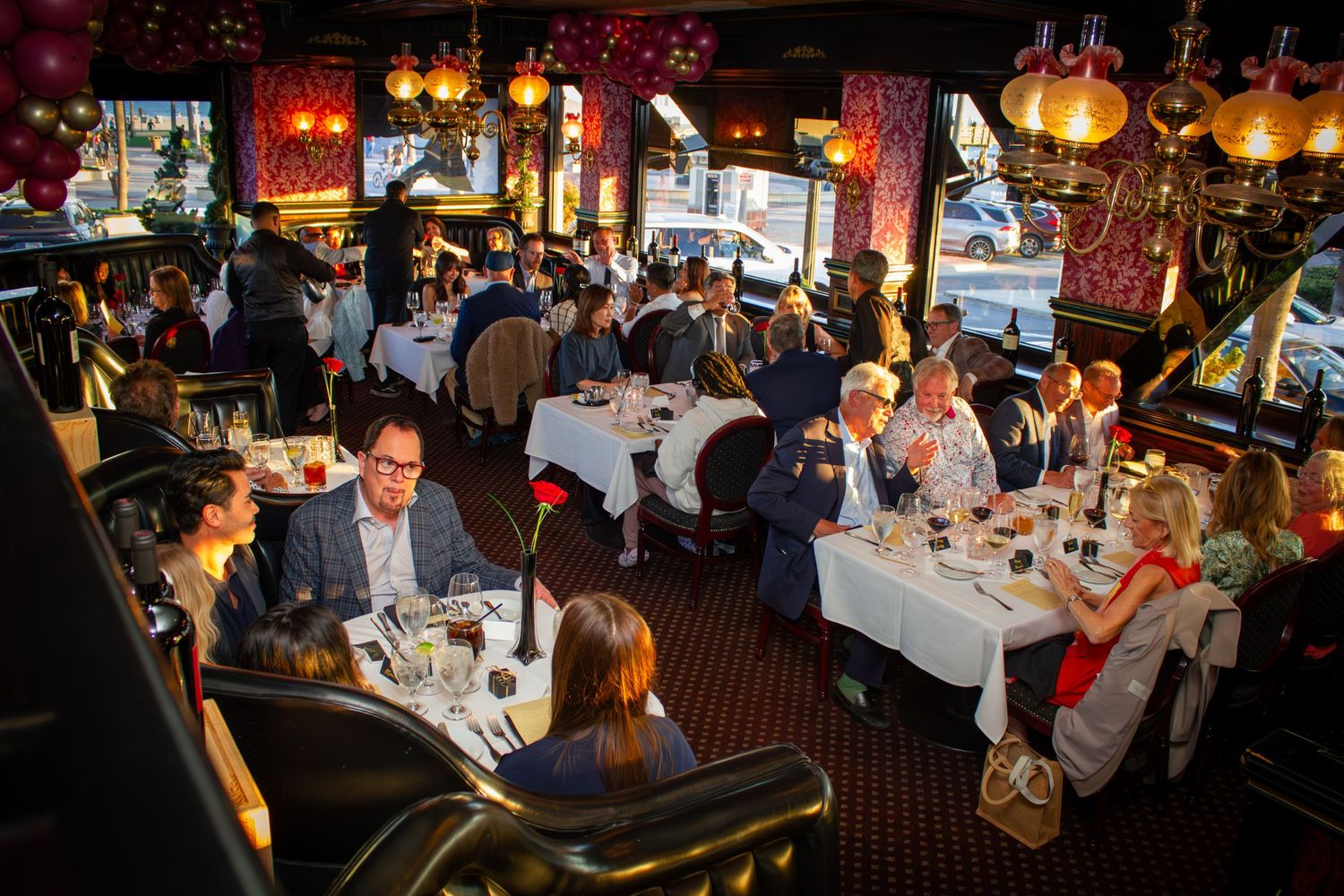 Elegantly dressed guests dine at white-clothed tables in a lavishly decorated restaurant with colorful lanterns.