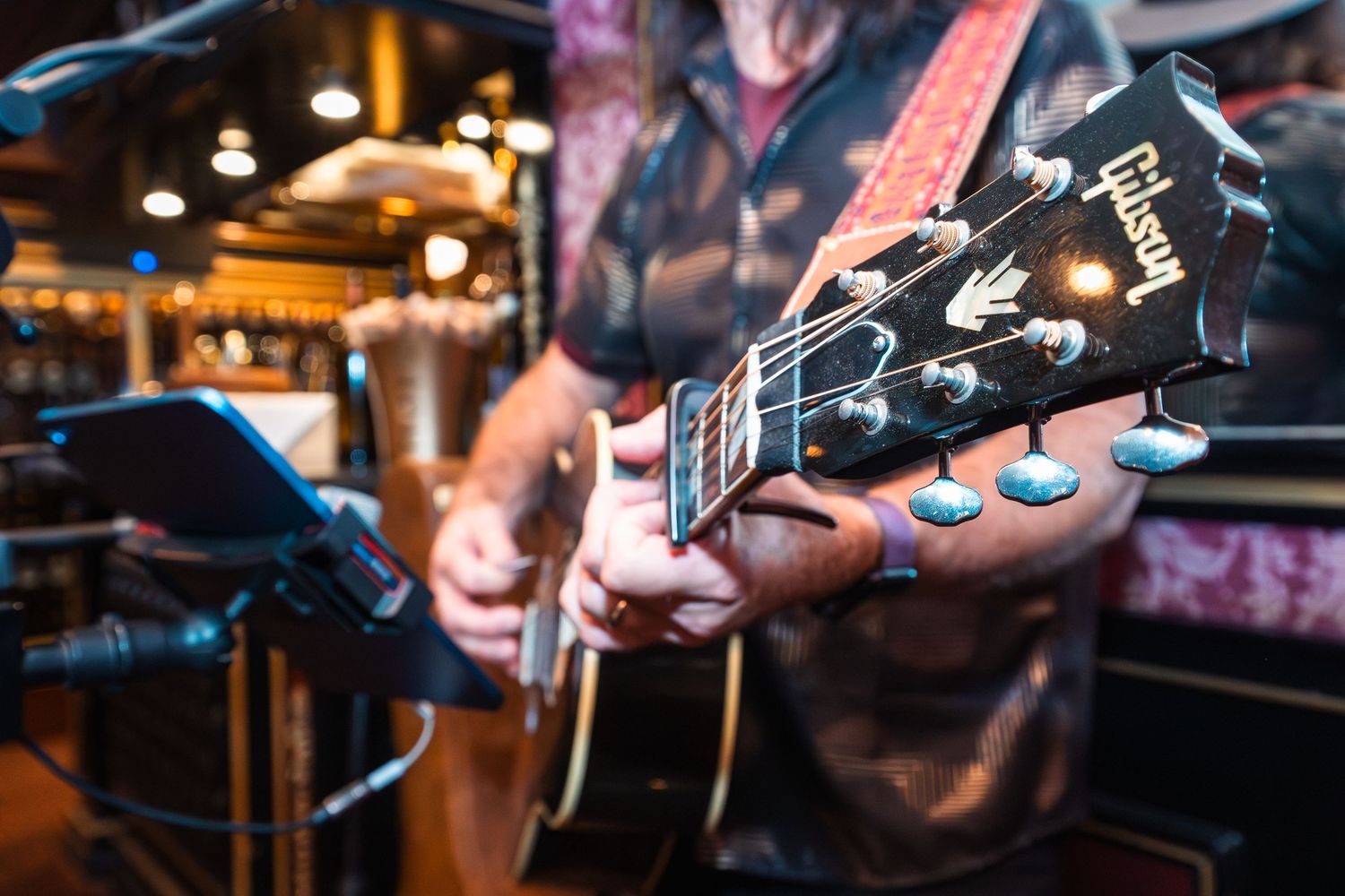 Close-up of a musician playing a Gibson acoustic guitar on stage in a warmly lit venue.