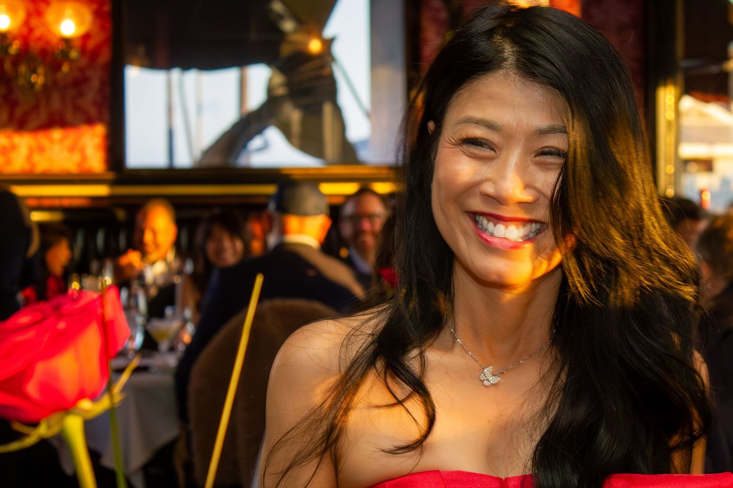 Smiling woman in red dress with long dark hair wearing a necklace at an elegant restaurant event.