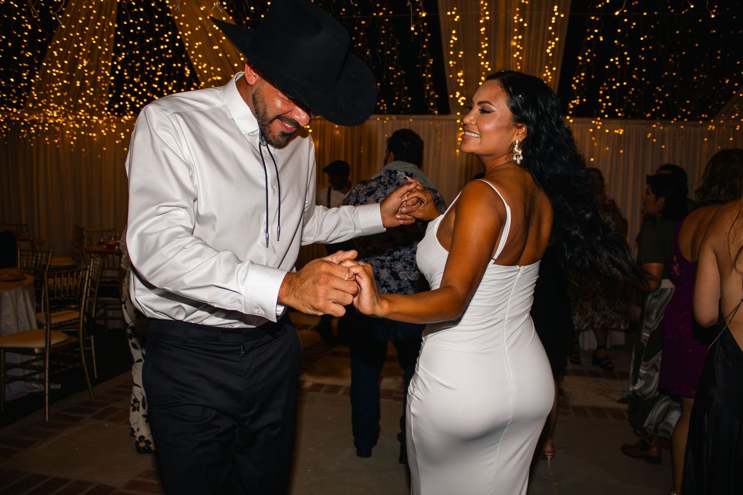 Couples dancing under romantic string lights at an evening wedding celebration.