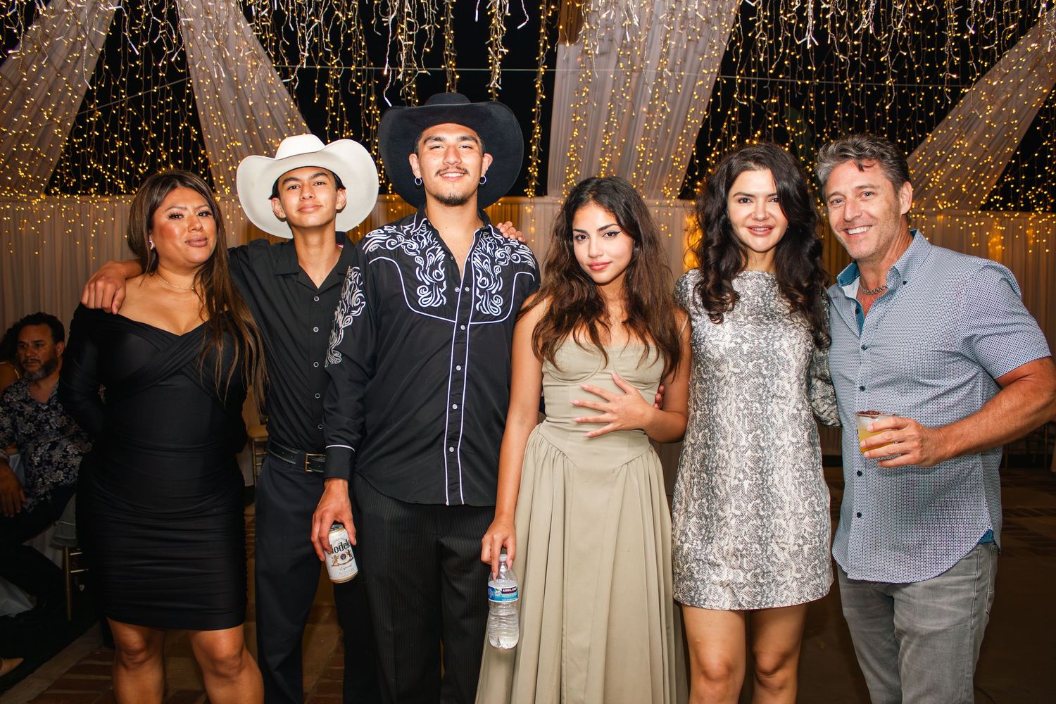 Party guests pose together against a sparkling gold backdrop at an evening celebration.