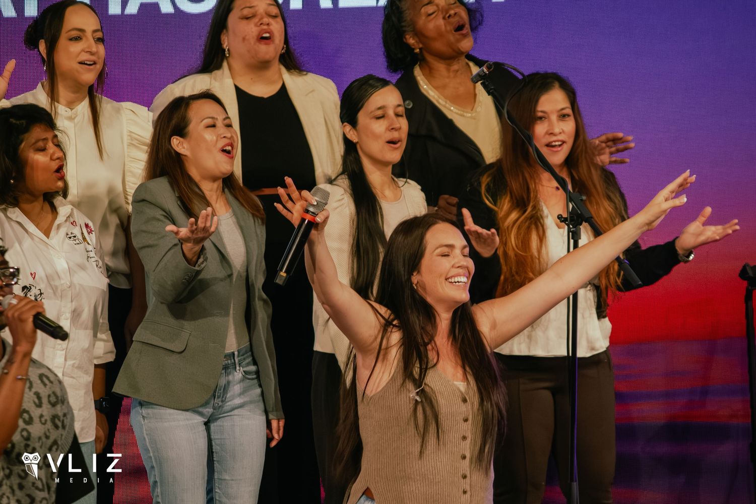Group of women singing and performing on a colorful lit stage at a live event.