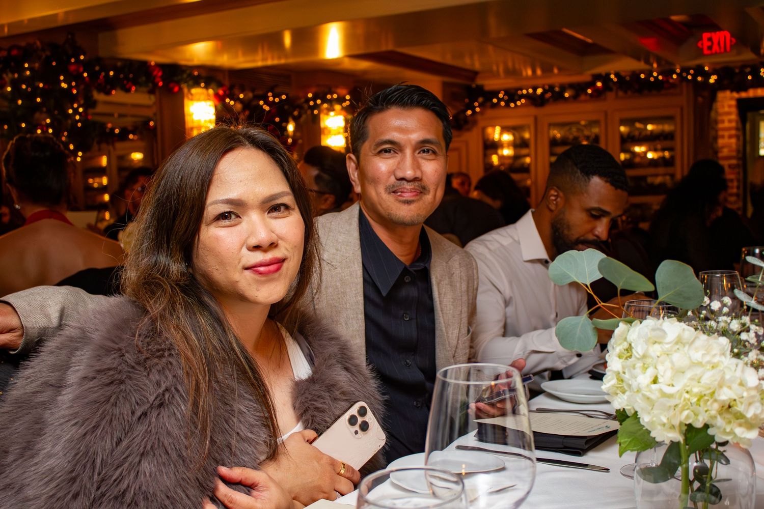 Couple dining at elegant restaurant with white floral centerpiece and ambient lighting.