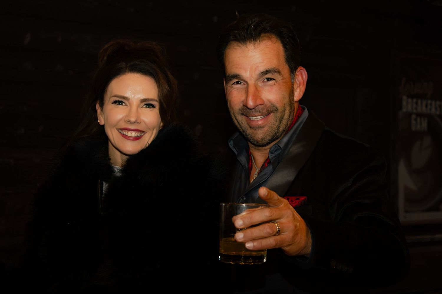 A couple smiles together at an upscale evening event in dark formal attire.