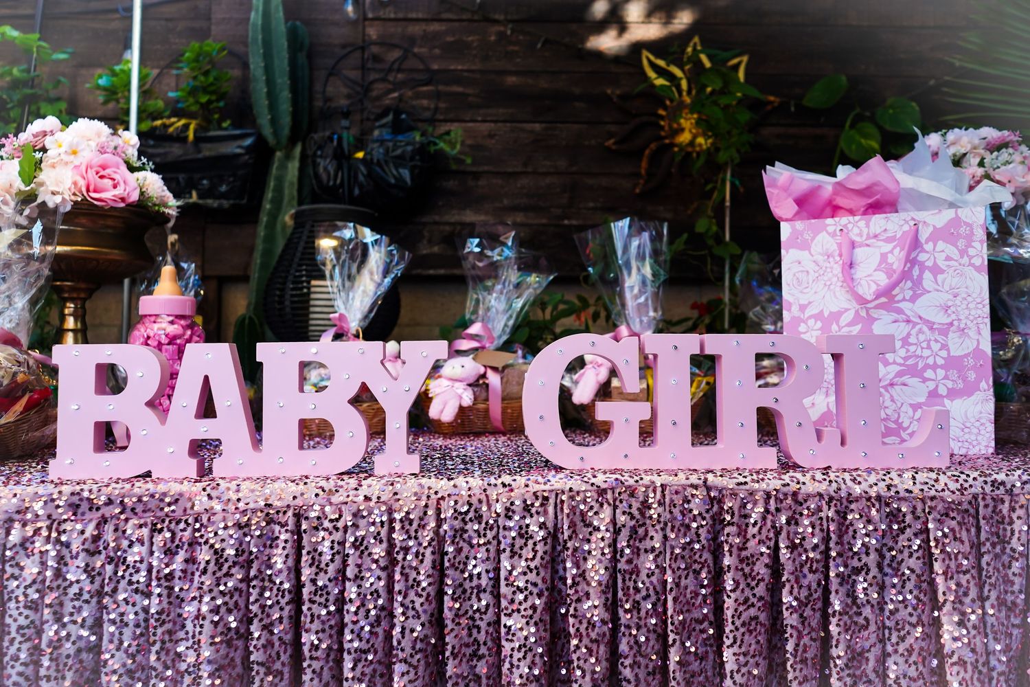 Pink 'BABY GIRL' letters displayed on sparkly pink tablecloth with gifts and decorations.