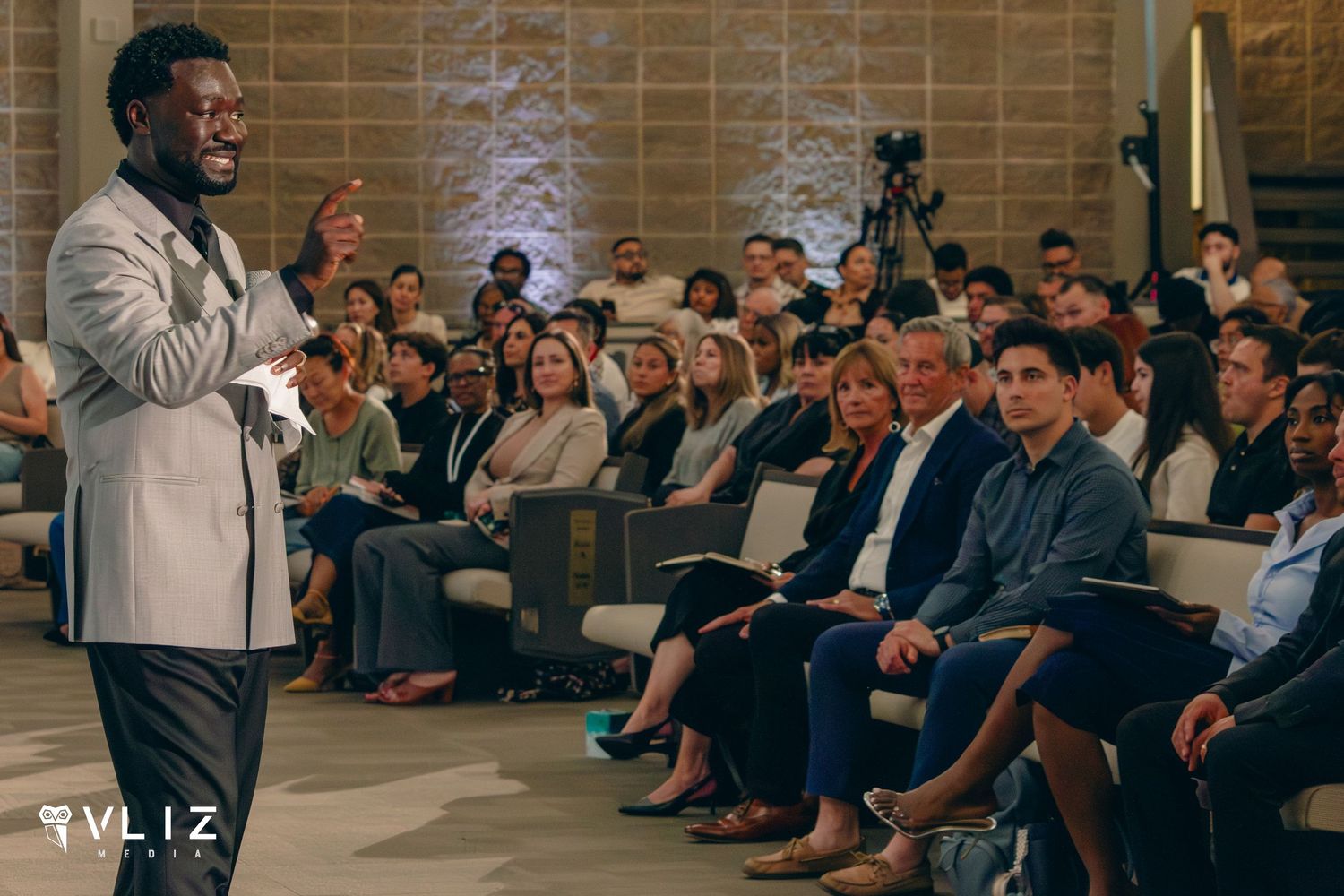 A dynamic speaker addresses a diverse, engaged audience in an elegant conference hall during a professional event.