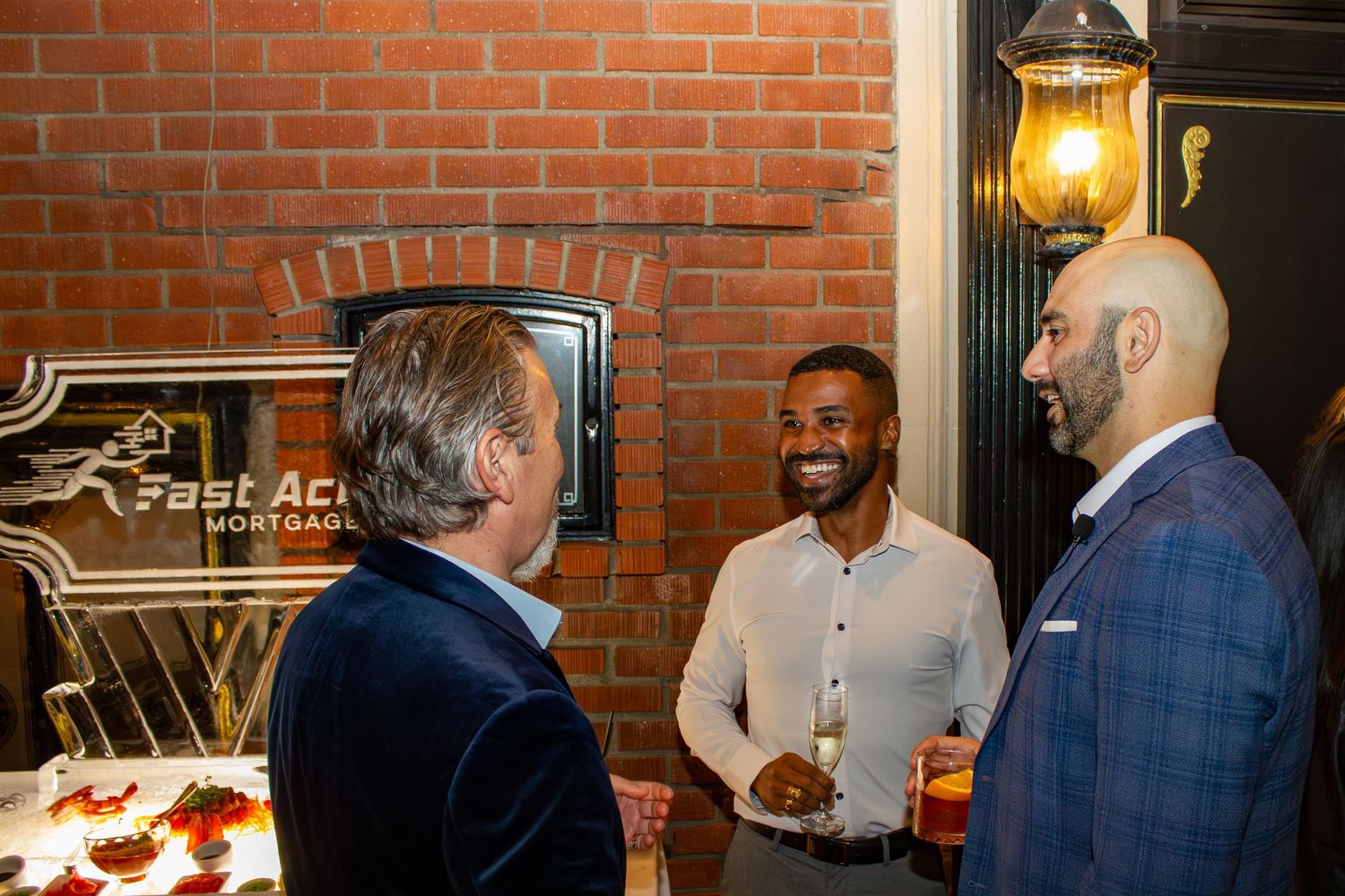 Three guests engage in conversation by Fast Action logo sign at corporate event.