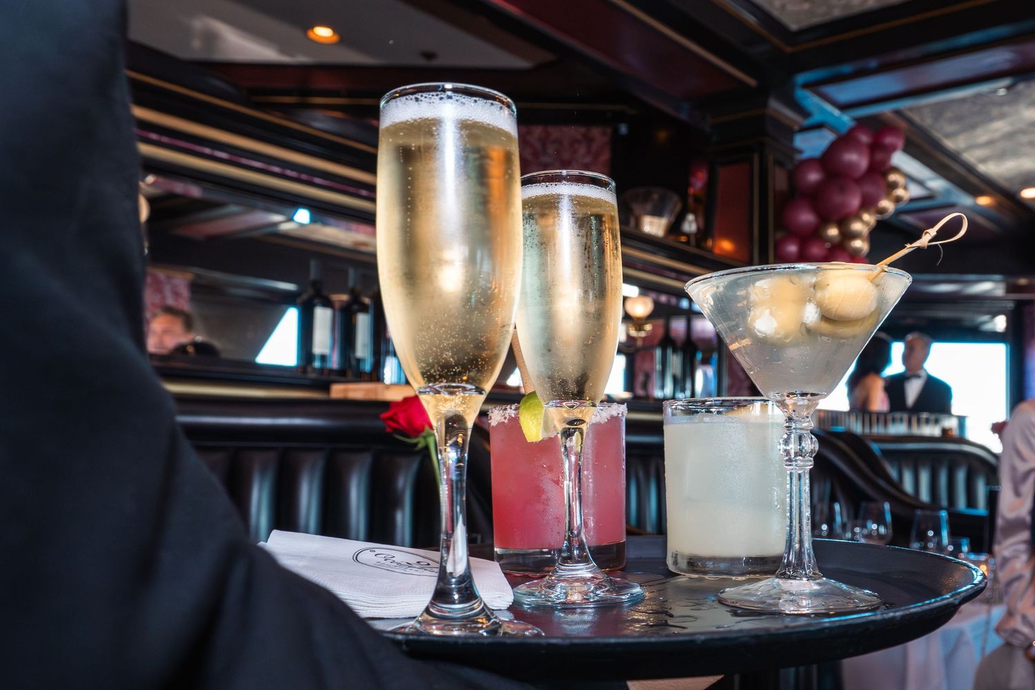 Elegant cocktails on a tray including champagne flutes and a martini with olives at an upscale bar.