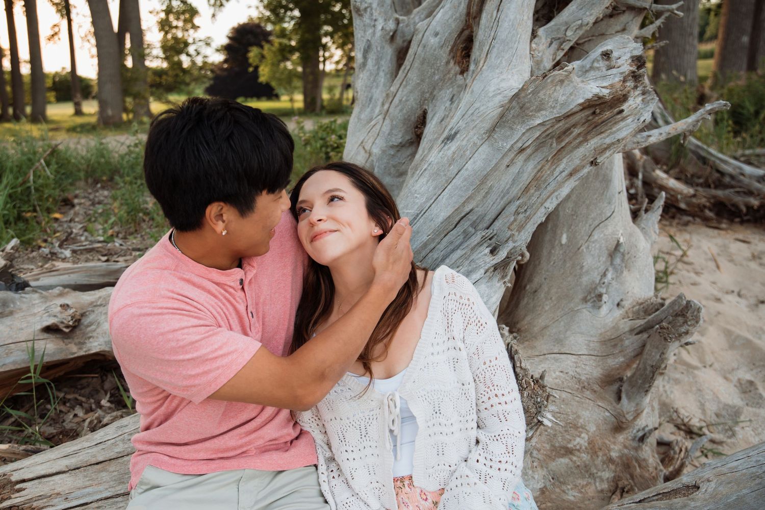 Couple sharing a romantic moment leaning against driftwood during golden hour engagement photography session.