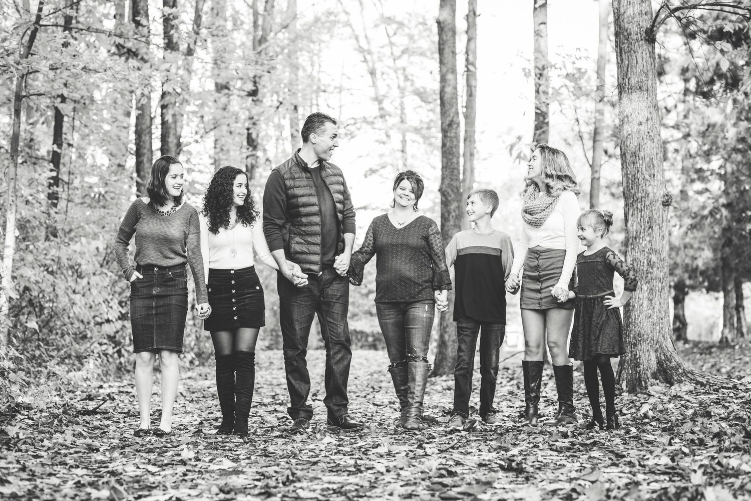 Black and white photo of seven family members walking together in autumn forest.