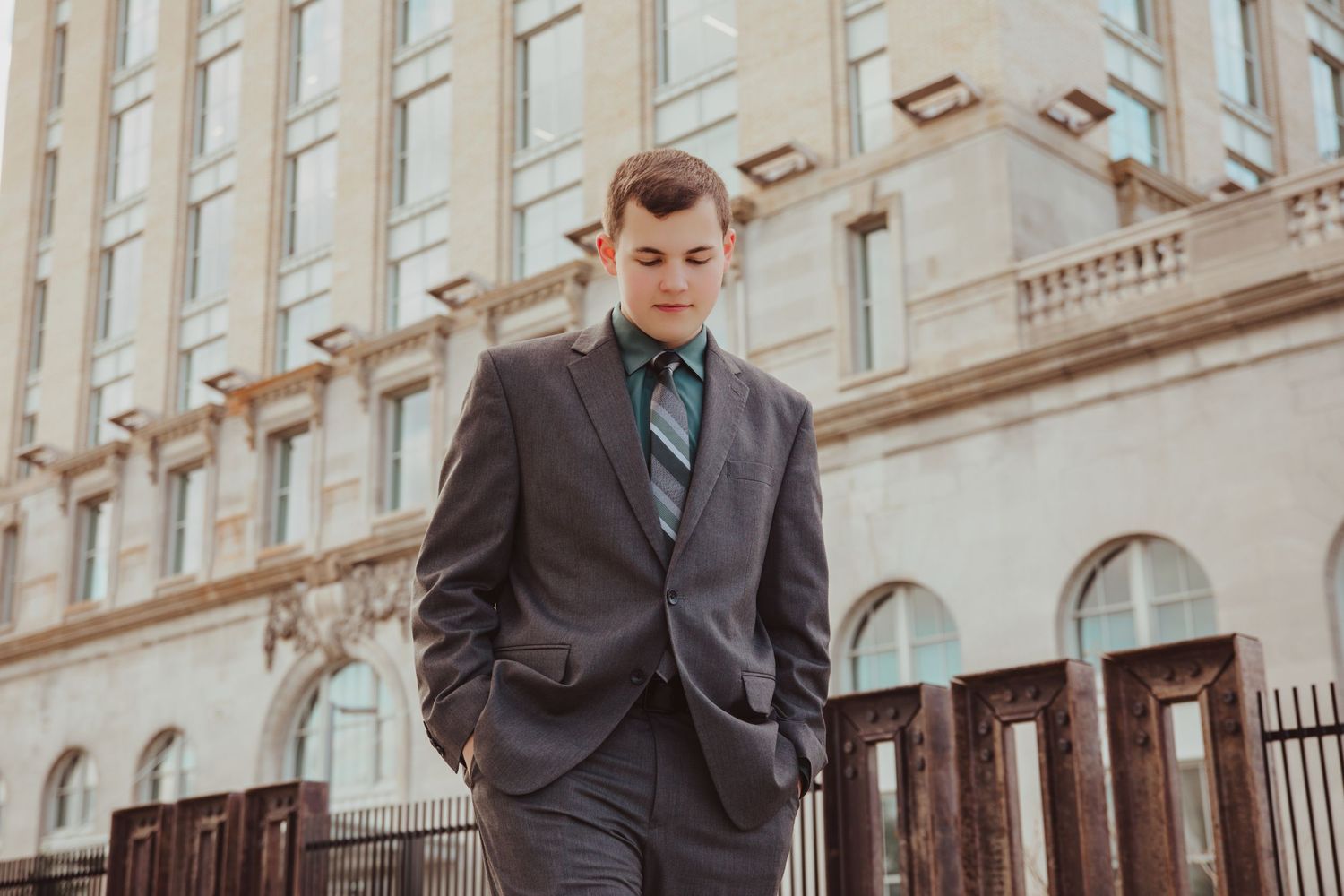 Young man in gray suit and striped tie standing confidently outside a classic stone building.