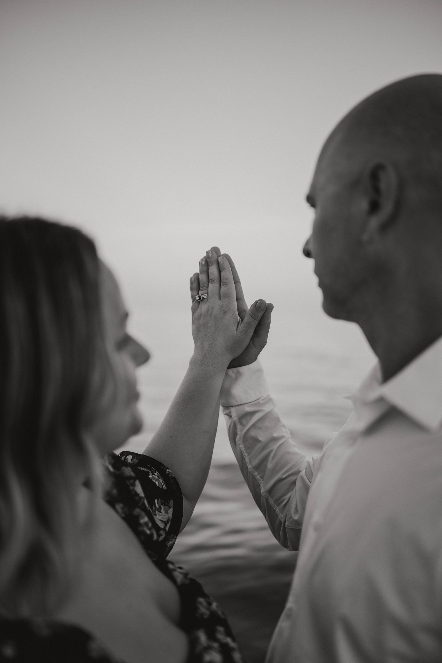 Black and white close-up of an engaged couple pressing their hands together showing an engagement ring.