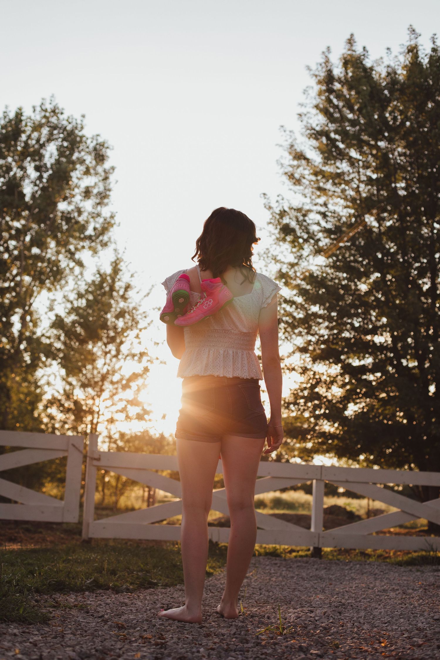 Silhouette of young woman holding pink flowers at sunset near white fence.