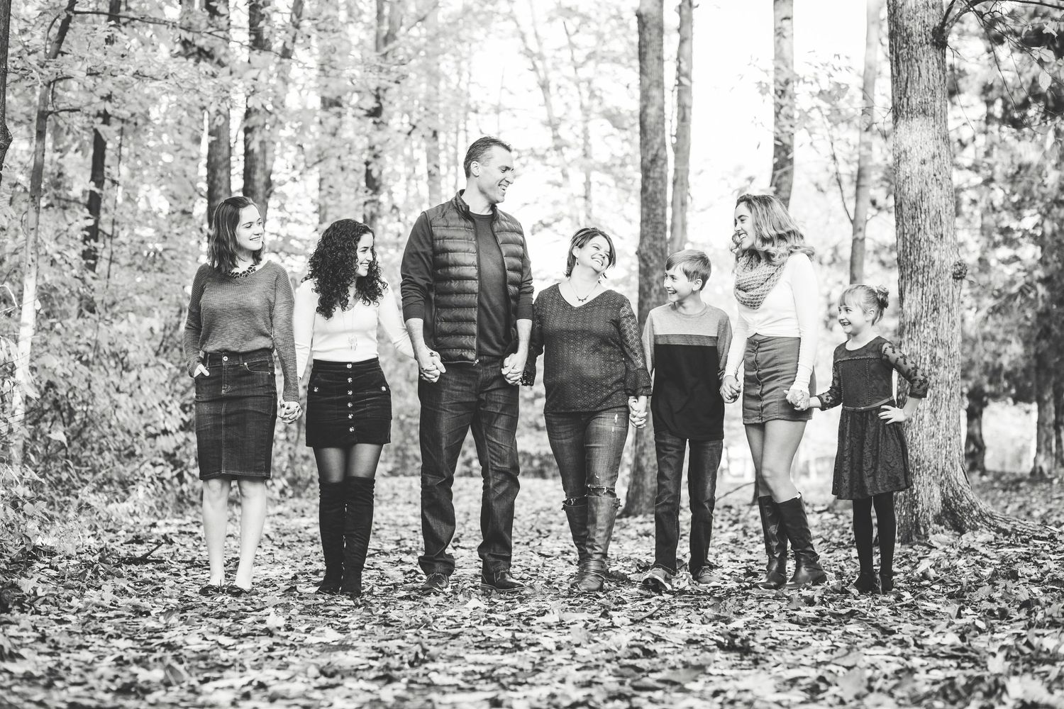 Black and white photo of a family of seven walking together through an autumn forest covered in fallen leaves.